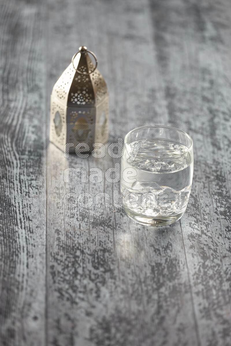 A silver lantern with different drinks, dates, nuts, prayer beads and quran on grey wooden background