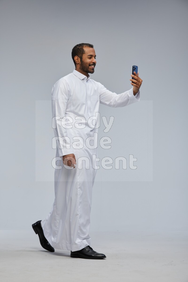 Saudi man wearing Thob standing taking selfie on Gray background