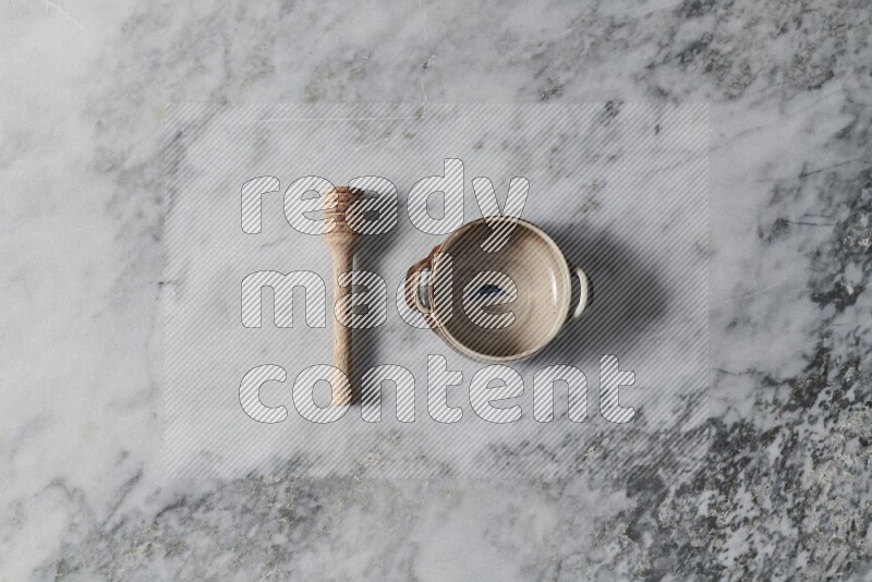 Multicolored pottery bowl with wooden honey dipper on the side on grey marble background