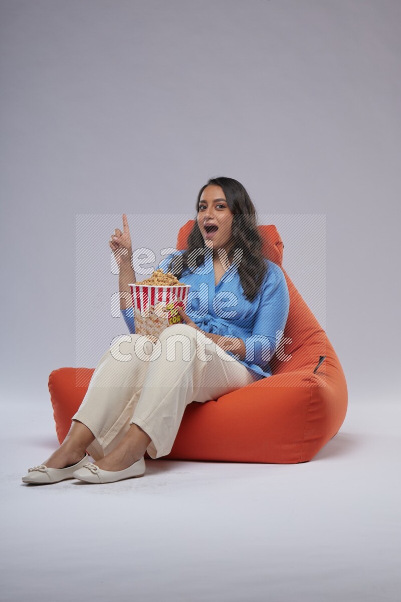 A woman sitting on an orange beanbag and eating popcorn