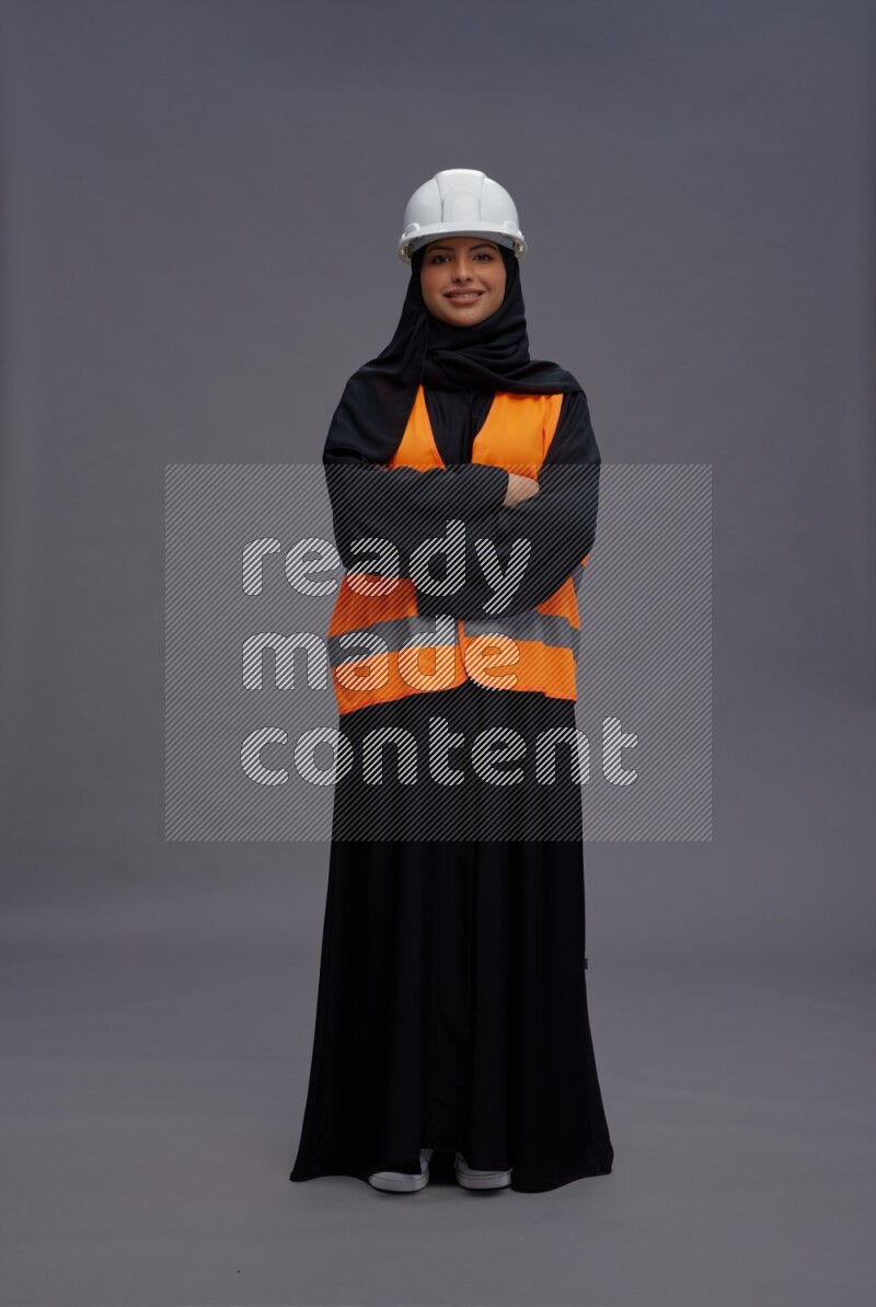 Saudi woman wearing Abaya with engineer vest standing with crossed arms on gray background