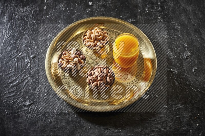 مكسرات في أطباق معدنية مع مشروب قمر الدين على صينية علي خلفية سوداء