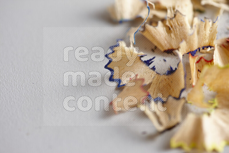 A close-up showing a small pile of pencil shavings with varied color edges on grey background