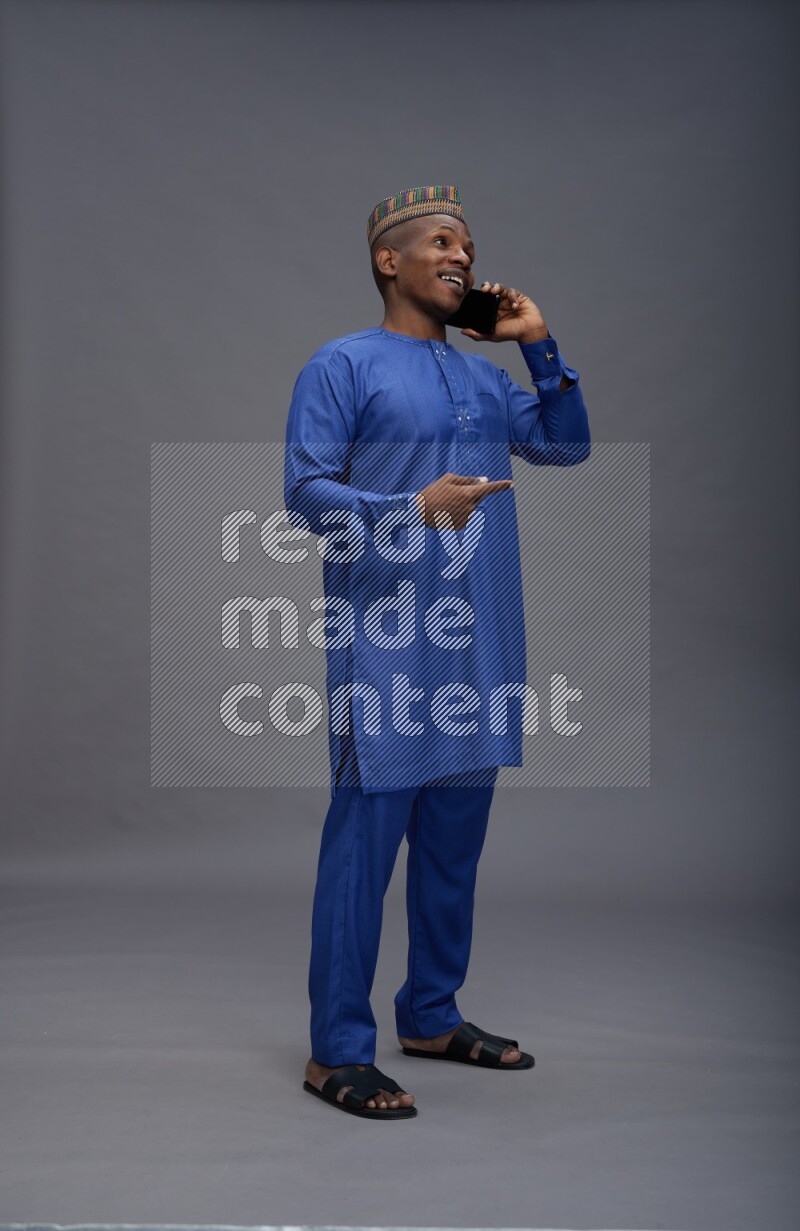 Man wearing Nigerian outfit standing talking on phone on gray background