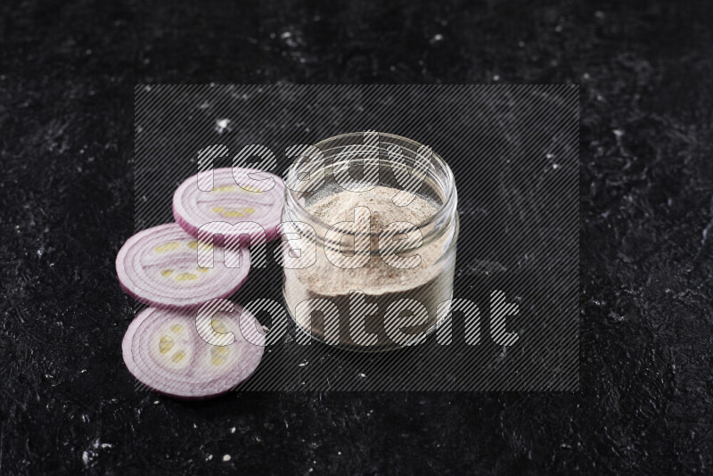 A glass jar full of onion powder on black background