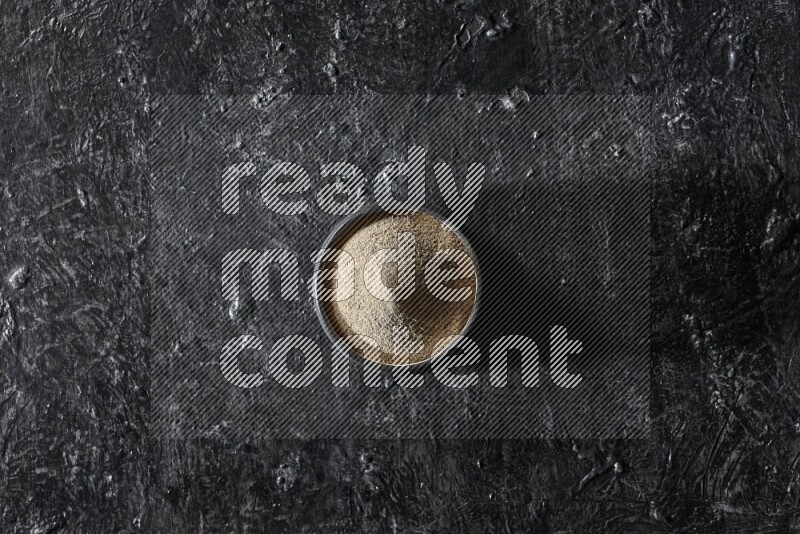 Black pottery bowl full of white pepper powder on textured black flooring