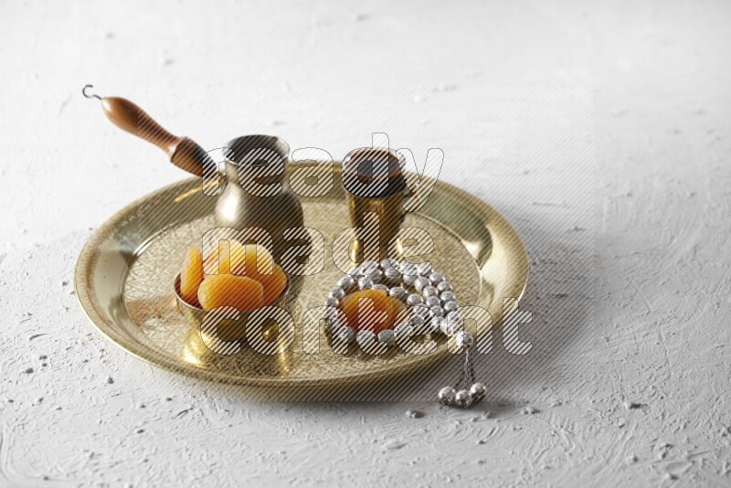 Dried apricots in a metal bowl with coffee and prayer beads on a tray in a light setup