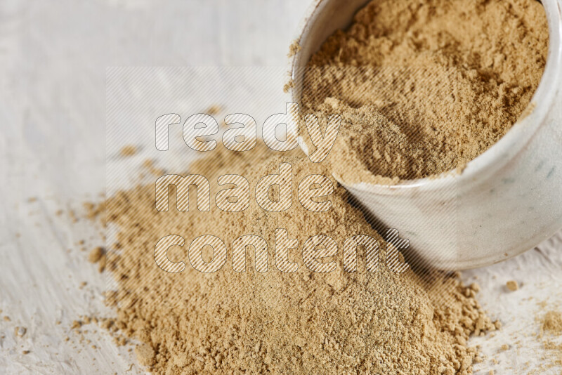 A beige pottery bowl full of ground ginger powder with fallen powder from it on white background