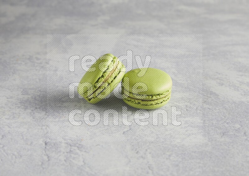 45º Shot of two Green Pistachio macarons  on white  marble background