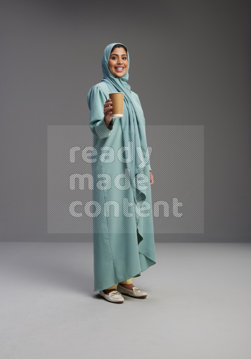 Saudi Woman wearing Abaya standing  holding paper cup on Gray background