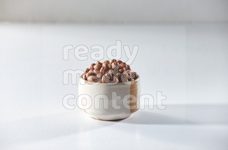 A beige ceramic bowl full of peeled hazelnuts on a white background in different angles