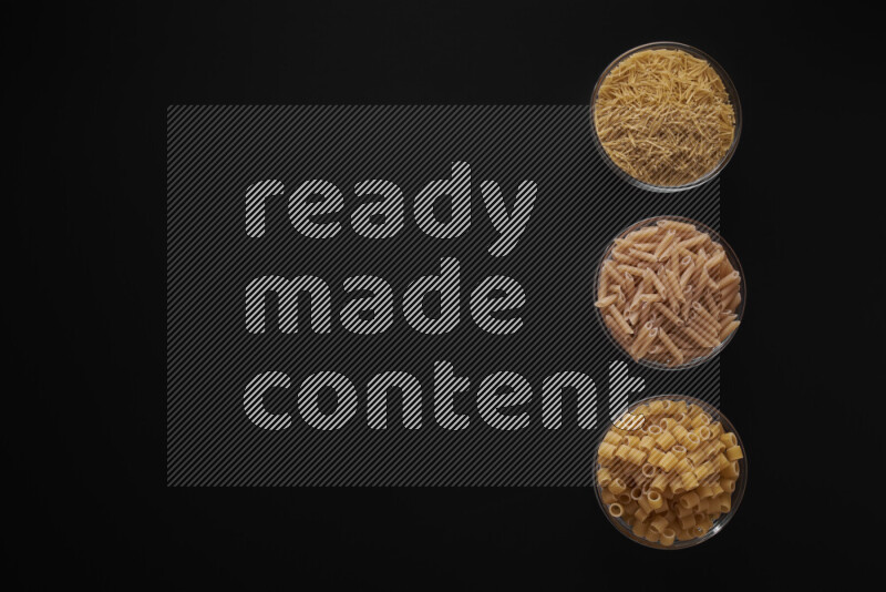 Different pasta types in 3 glass bowls on black background
