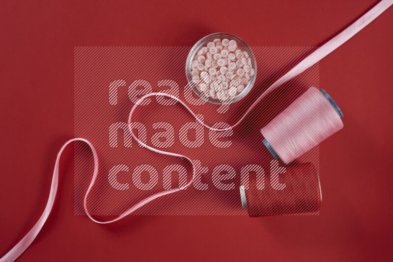 A pink and red collection of sewing and tailoring tools arranged on a red background