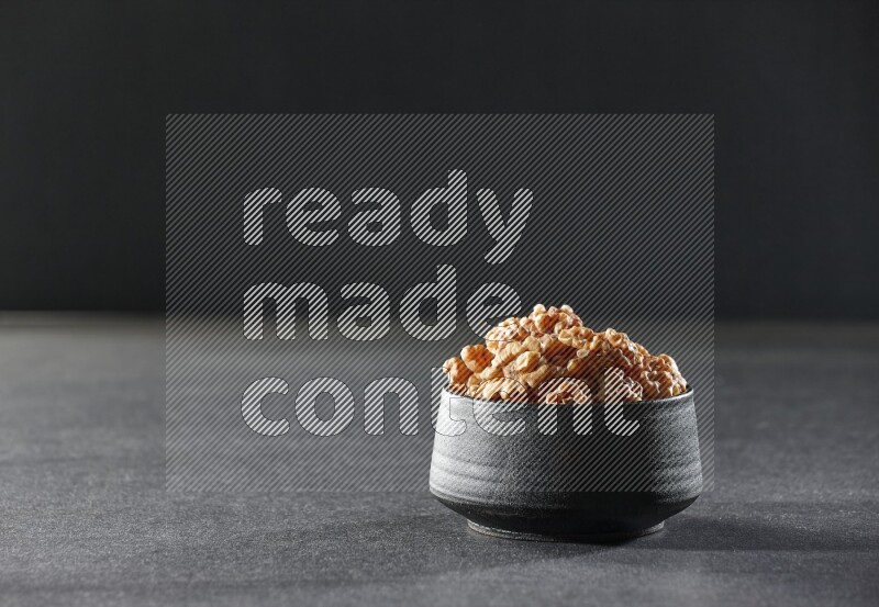 A black pottery bowl full of peeled walnuts on a black background in different angles