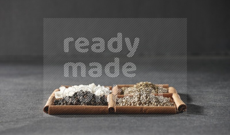 4 مربعات من عيدان القرفة ممتلئة بحبوب الفلفل الأسود والكمون وحبوب الفلفل الأبيض والملح الأبيض على أرضية سوداء