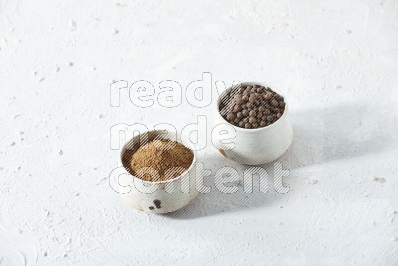 2 beige bowls, one full of allspice powder and the other full of whole balls on a textured white flooring