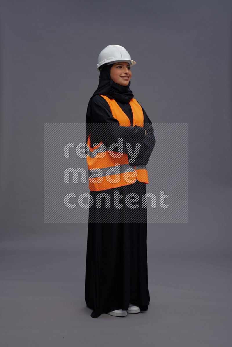 Saudi woman wearing Abaya with engineer vest standing with crossed arms on gray background