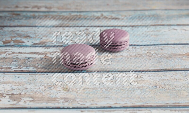 45º Shot of two Purple Blueberry macarons on light blue wooden background