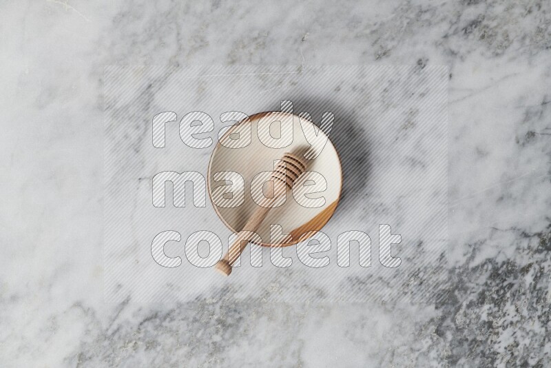 Multicolored pottery plate with wooden honey dipper in it on grey marble background