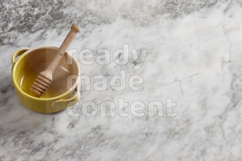 Multicolored pottery bowl with wooden honey dipper in it on grey marble background