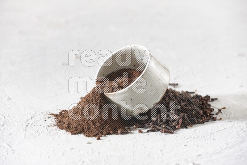 A beige ceramic bowl with cloves powder spilled out of it on a textured white flooring