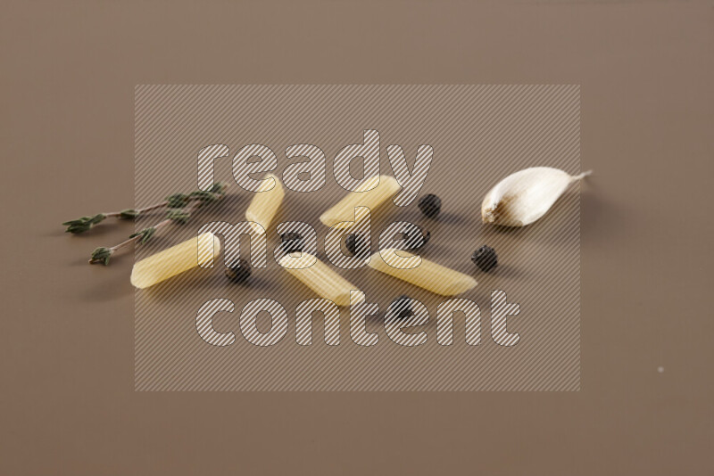 Raw pasta with different ingredients such as cherry tomatoes, garlic, onions, red chilis, black pepper, white pepper, bay laurel leaves, rosemary and cardamom on beige background