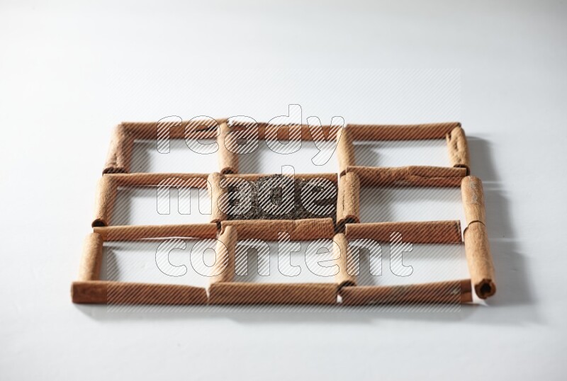 9 مربعات من أعواد القرفة ممتلئة بالشاي في المنتصف محاطة بجوزة الطيب والنعناع المجفف والقرنفل والريحان المجفف والزنجبيل المجفف والقرفة واليانسون والهيل على أرضية بيضاء