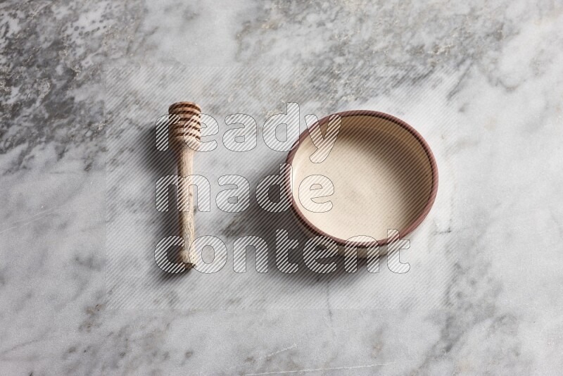 Beige pottery oven bowl with wooden honey dipper on the side on grey marble background