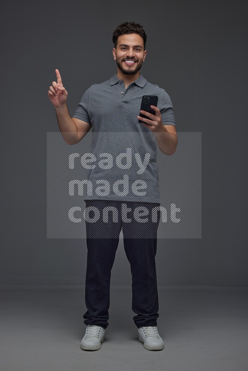 A man wearing casual standing and using his phone and making multi hand gestures eye level on a gray background