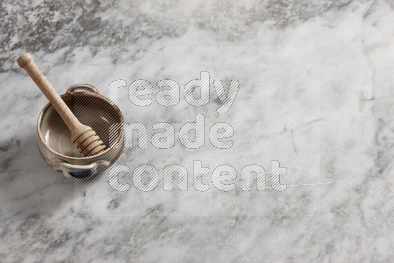 Multicolored pottery bowl with wooden honey dipper in it on grey marble background