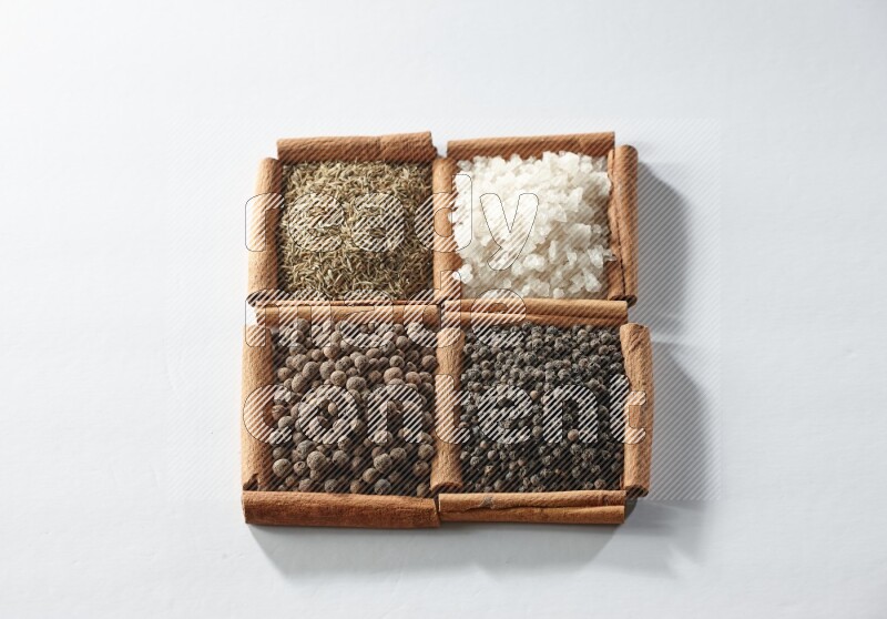 4 مربعات من أعواد القرفة ممتلئة بالكمون والملح الأبيض وبهار الفلفل الحلو وحبوب الفلفل الأسود على أرضية بيضاء