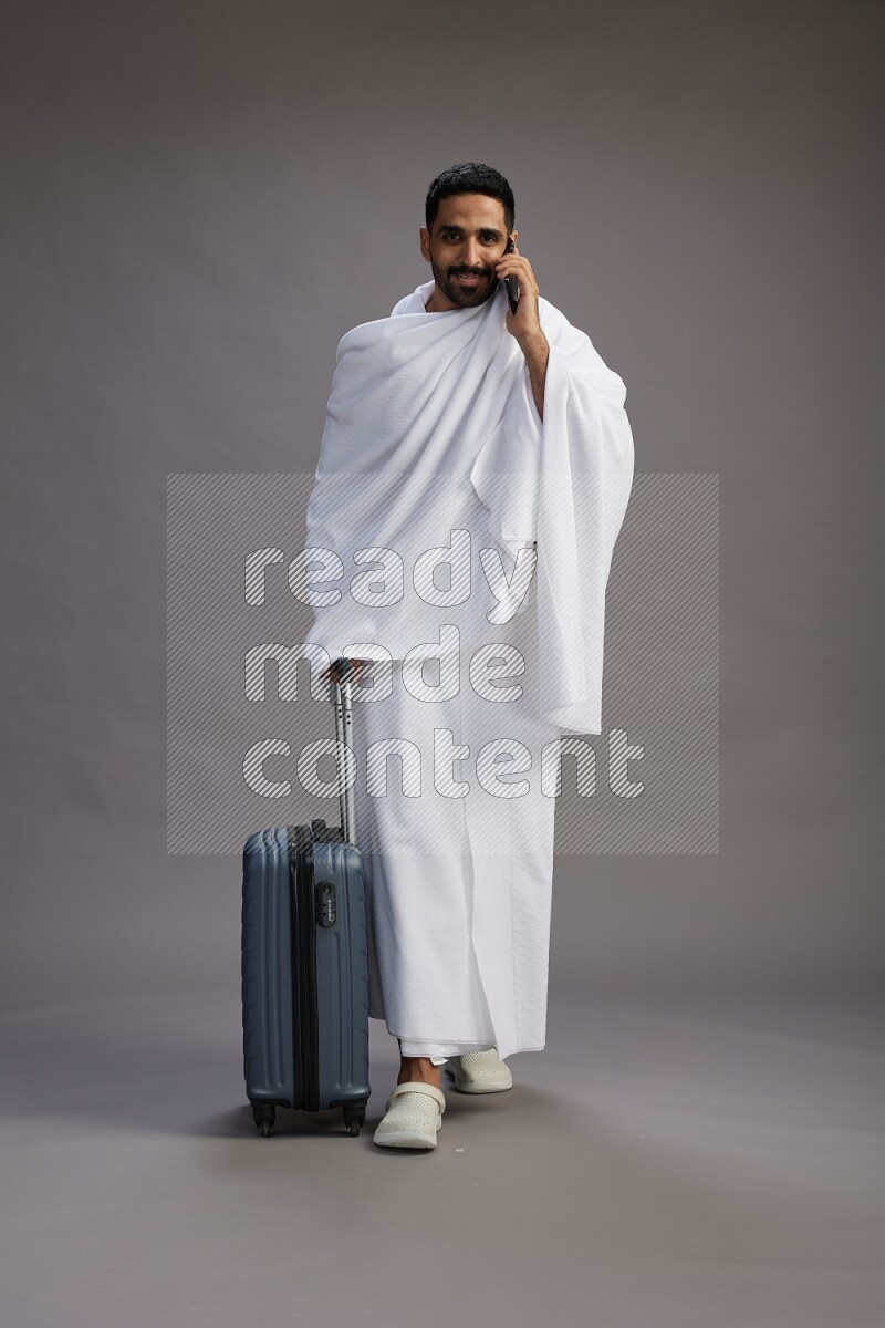 A man wearing Ehram Standing holding traveling bag on gray background