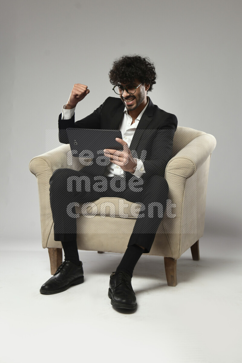 رجل يرتدي ملابس رسمية يجلس علي كرسي و يلعب علي تابلت علي خلفية بيضاء