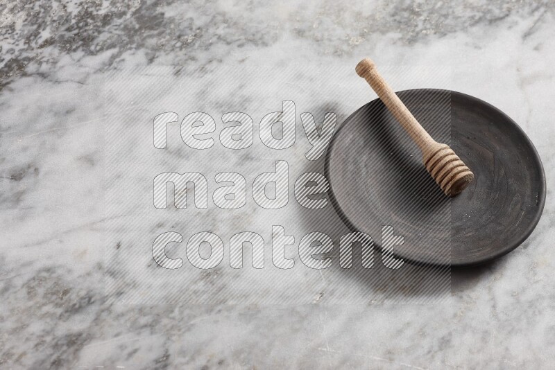 Black pottery plate with wooden honey dipper in it on grey marble background