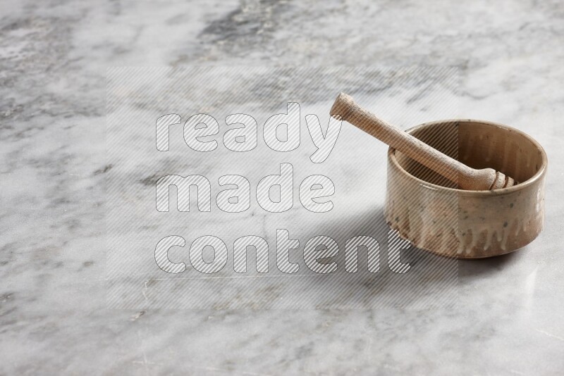 Beige pottery bowl with wooden honey dipper in it on grey marble background