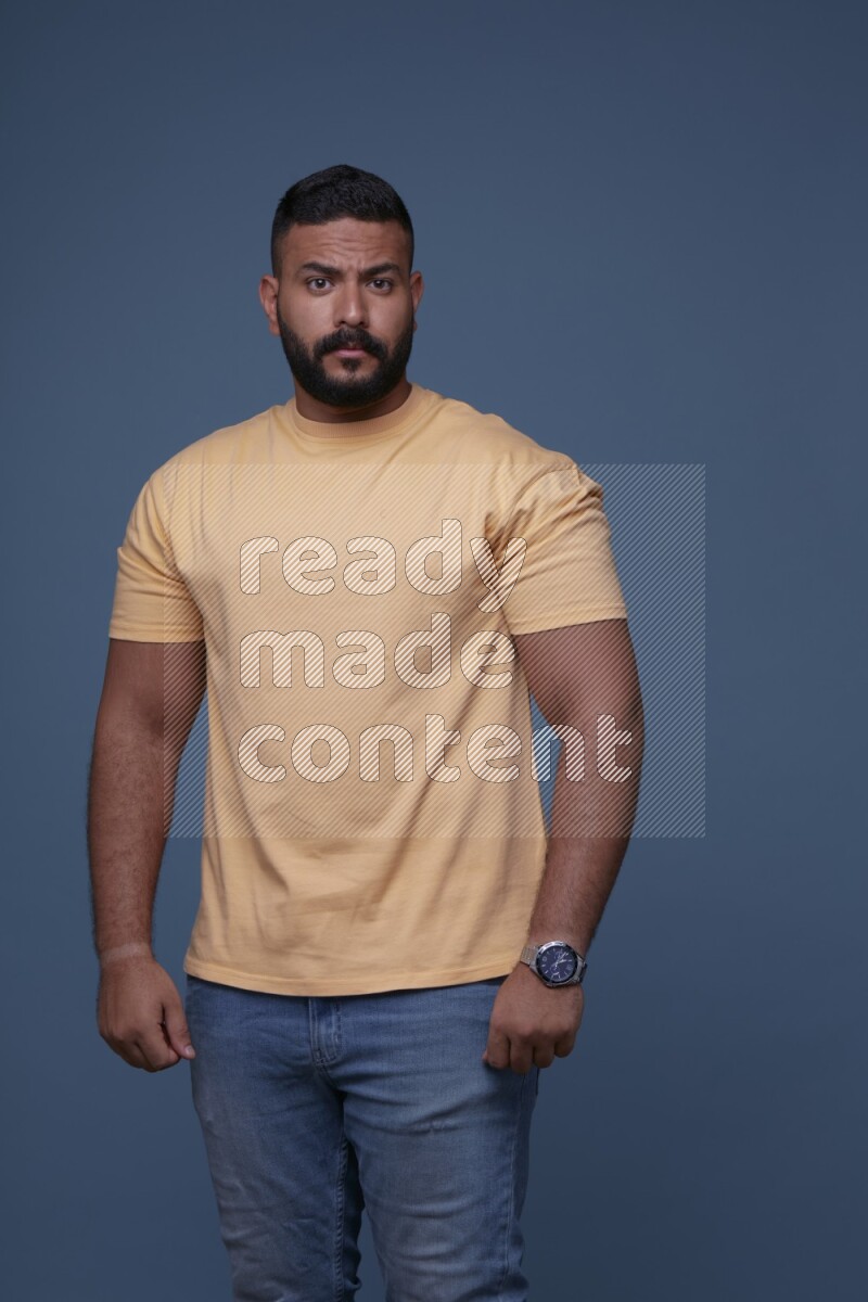 A man posing in a blue background wearing a yellow shirt