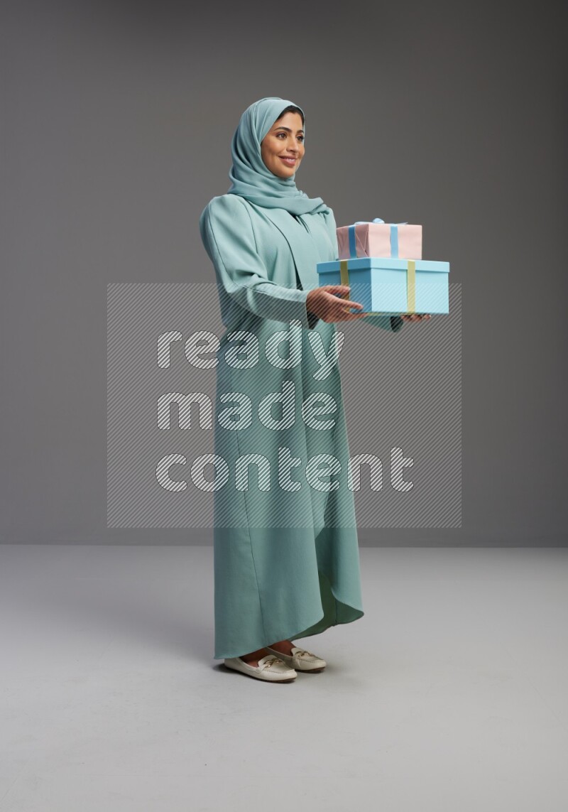 Saudi Woman wearing Abaya standing holding gift box on Gray background