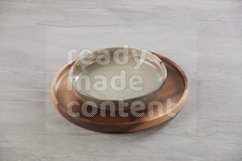 multi color pottery round dish on top of brown wood round plate and spoon, on grey textured countertop