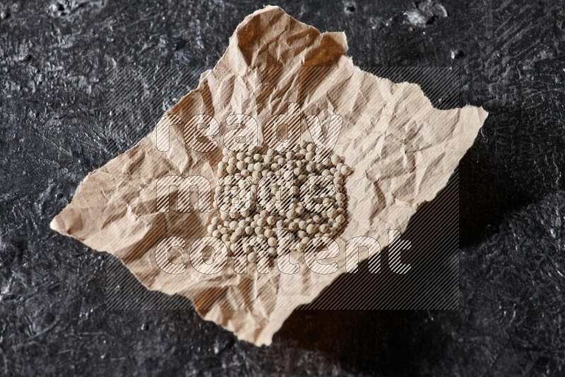 White pepper beads in a crumpled piece of on textured black flooring