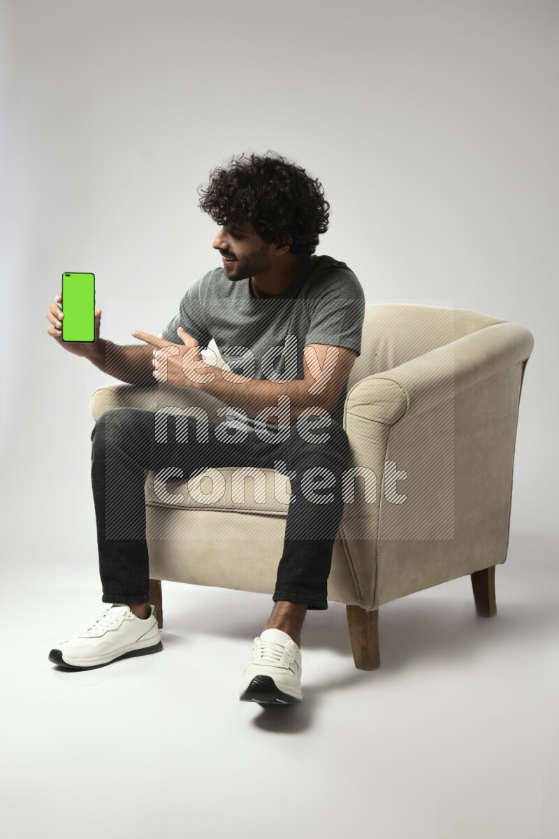 A man wearing casual sitting on a chair showing a phone screen on white background