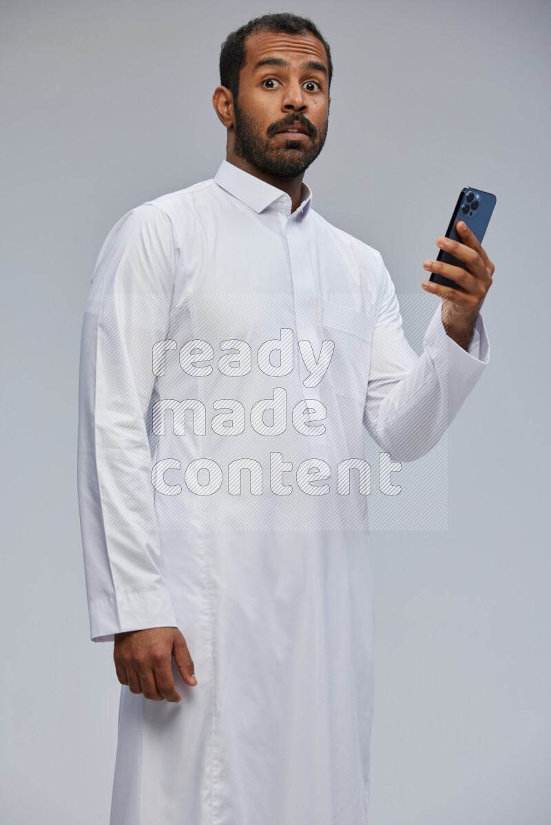 Saudi man wearing Thob standing texting on phone on Gray background