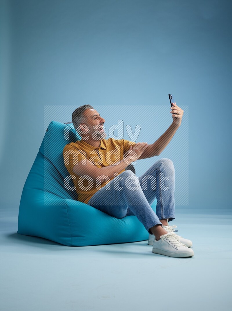 A man sitting on a blue beanbag and taking selfie