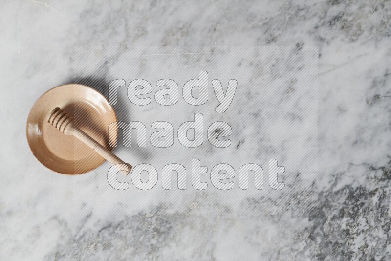 طبق فخاري بيج مع ملعقة عسل خشبية بداخله على خلفية من الرخام الرمادي