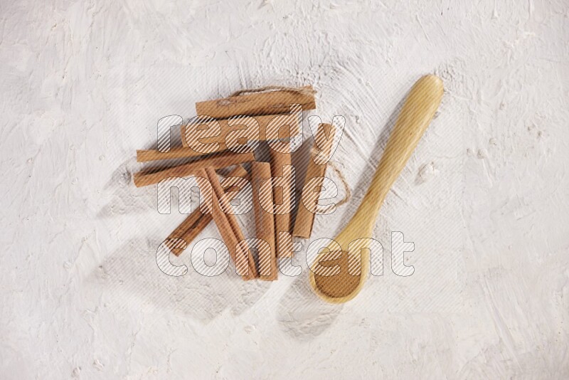 Cinnamon sticks stacked beside a wooden spoon full of cinnamon powder on white background