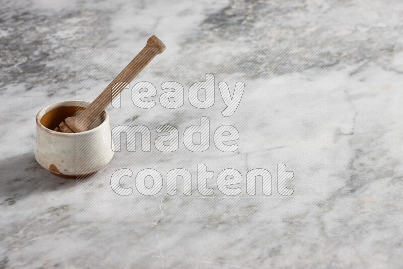 Beige pottery bowl with wooden honey dipper in it on grey marble background
