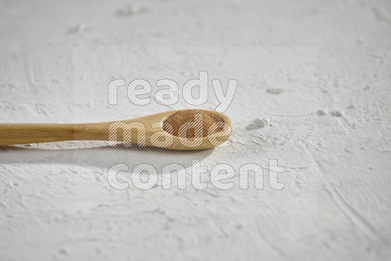 Cinnamon powder in a wooden spoon on a white background