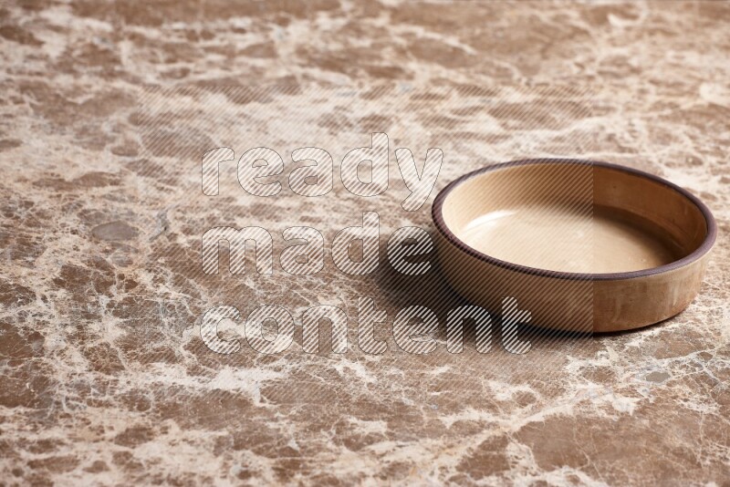 A beige pottery oven plate on beige marble background