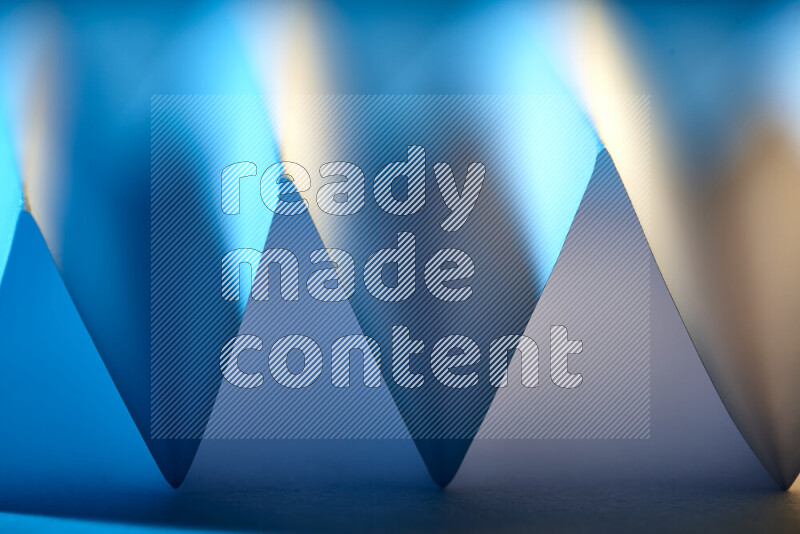 A close-up abstract image showing sharp geometric paper folds in blue gradients and warm tones