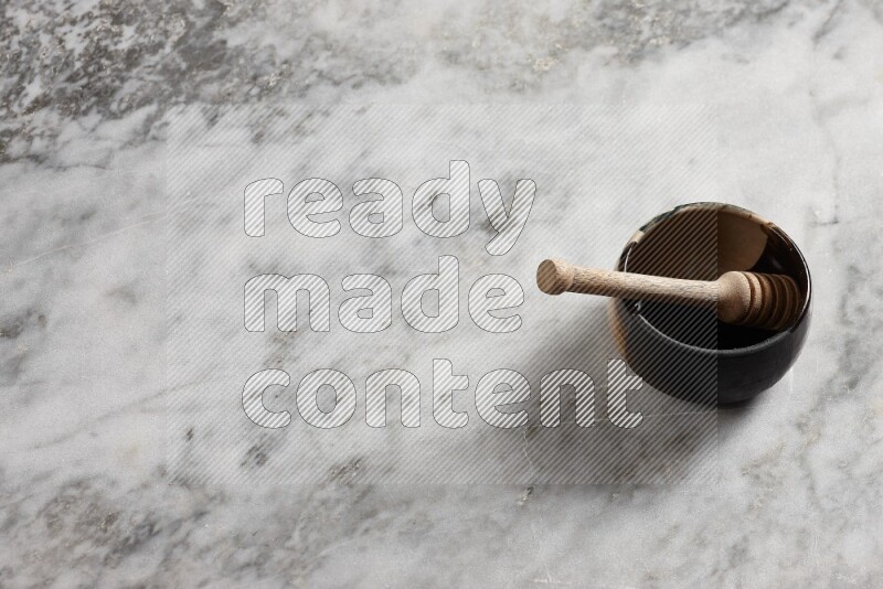 Multicolored pottery bowl with wooden honey dipper in it on grey marble background
