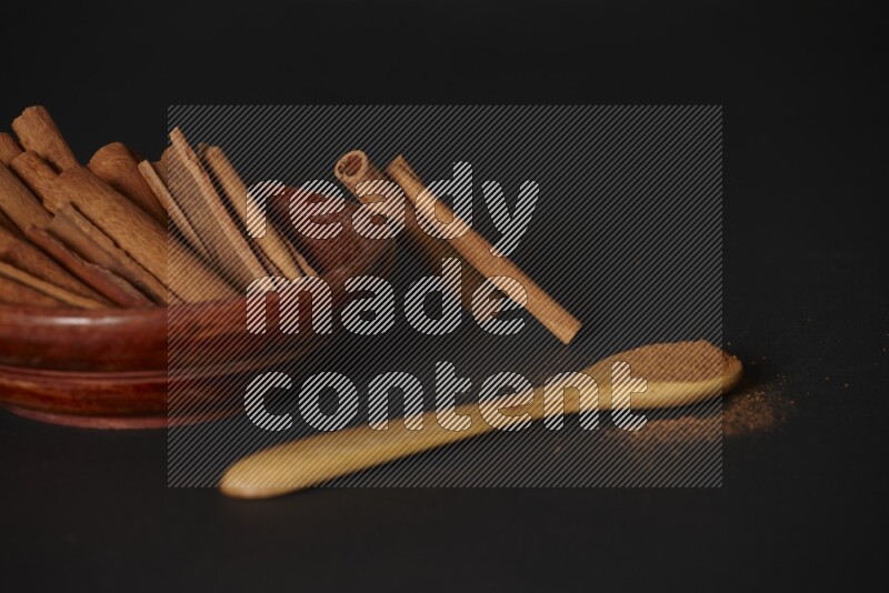 Cinnamon sticks in wooden bowl and cinnamon powder in a wooden spoon on black background